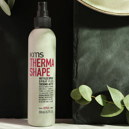 KMS Thermo Shape hair spray bottle with green leaves on a dark background