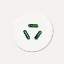 Three green capsules on a white circular platform with a white background