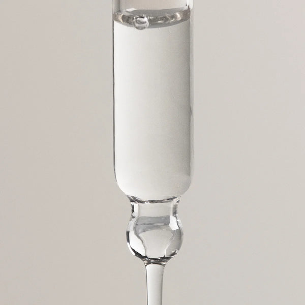 A clear glass dropper pipette containing a white liquid, shown vertically against a neutral light gray background.