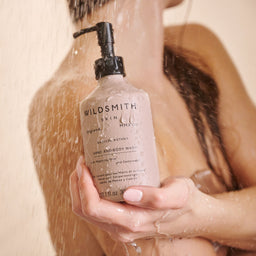 Person holding a bottle of Wildsmith hand and body wash under running water.