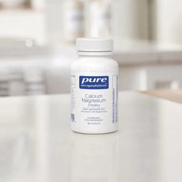 Bottle of Pure Encapsulations Calcium Magnesium supplement on a white surface with a blurred background