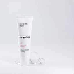 A tube of mesoestetic Anti-Stress Mask with three glass orbs behind it