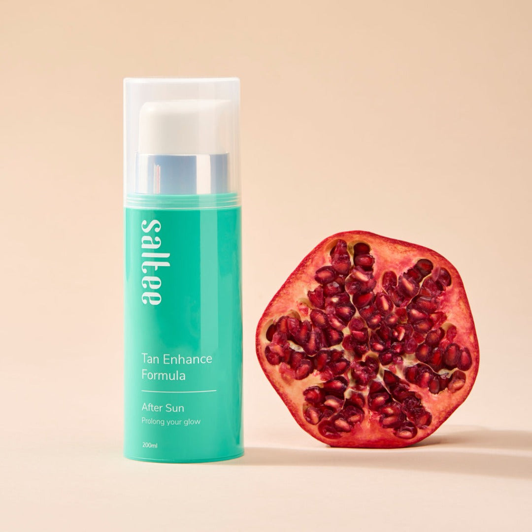 a bottle of Saltee Tan Enhance Formula next to half a pomegranate 