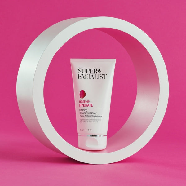 Creamy cleanser tube inside a white circular prop  against a bright pink backdrop