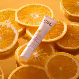 Vitamin C eye cream tube on top of sliced oranges on orange mirror table