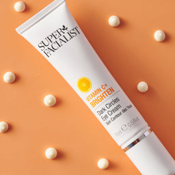 Vitamin C eye cream tube on orange background with eye cream drops around it